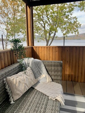 A covered outdoor seating area with wicker furniture and a view of a lake.