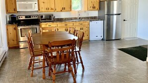 A kitchen with wooden cabinets, a stainless steel refrigerator, a microwave, an oven, and a dining table with chairs.