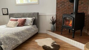 A bedroom with a bed, a rug, a fireplace, and a brick wall.