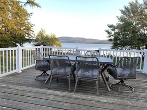 A deck with a table and four chairs, overlooking a body of water and hills. - A Peaceful Waterfront Escape | La Perle du Lac (Dégelis)