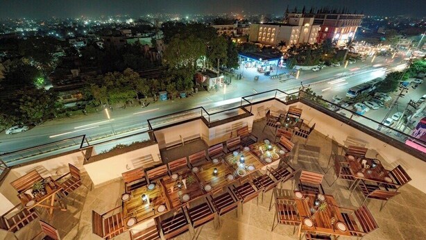 A rooftop restaurant with outdoor seating, a view of the cityscape, and a well-lit street below. - Crimson Park Residency & Spa (Udaipur)