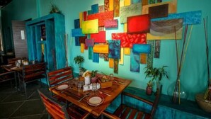 A dining area with a wooden table set for two, surrounded by chairs. A colorful abstract art installation adorns the wall behind the table. - Crimson Park Residency & Spa (Udaipur)