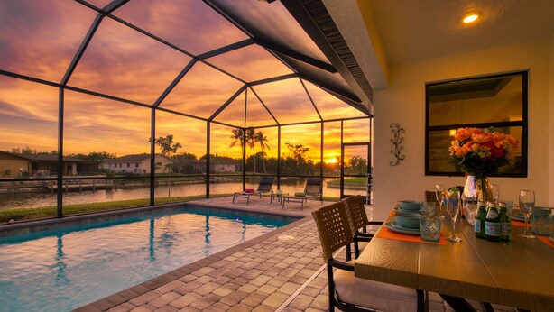 A covered outdoor area with a pool, seating, and a table set for dining. - VILLA MODERN TIMES – HEATED POOL | WATER VIEW | BOAT RENTAL + TOURS VOUCHER INCL. (Cape Coral)