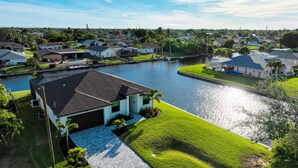A residential area with a house featuring a garage, a swimming pool, and a canal. - VILLA MODERN TIMES – HEATED POOL | WATER VIEW | BOAT RENTAL + TOURS VOUCHER INCL. (Cape Coral)