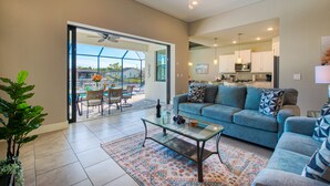 A spacious living area with a glass coffee table, a blue sofa, and a view of the outdoor patio. - VILLA MODERN TIMES – HEATED POOL | WATER VIEW | BOAT RENTAL + TOURS VOUCHER INCL. (Cape Coral)