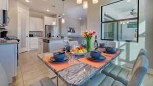 A modern kitchen with a marble island, pendant lighting, and a dining area with blue chairs and orange placemats. - VILLA MODERN TIMES – HEATED POOL | WATER VIEW | BOAT RENTAL + TOURS VOUCHER INCL. (Cape Coral)