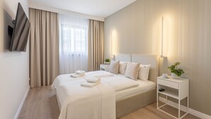 Moderni hotellihuone, jossa on suuri sänky, yöpöytä lampun kanssa ja seinälle asennettu taulutelevisio.