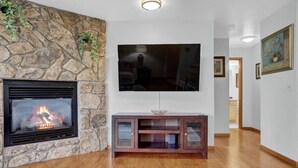 A living room with a stone fireplace, a flat-screen TV mounted on the wall, and a wooden entertainment center. - Pine Meadow Retreat (Steamboat Springs)
