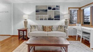 A living room with a sofa, coffee table, and a desk with a chair. There are two lamps on side tables. - Pine Meadow Retreat (Steamboat Springs)