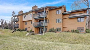 A multi-story wooden apartment building with balconies, a grassy front yard, and a clear sky. - Pine Meadow Retreat (Steamboat Springs)