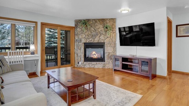 A living room with a stone fireplace, a flat-screen TV, a wooden coffee table, and a sofa. - Pine Meadow Retreat (Steamboat Springs)