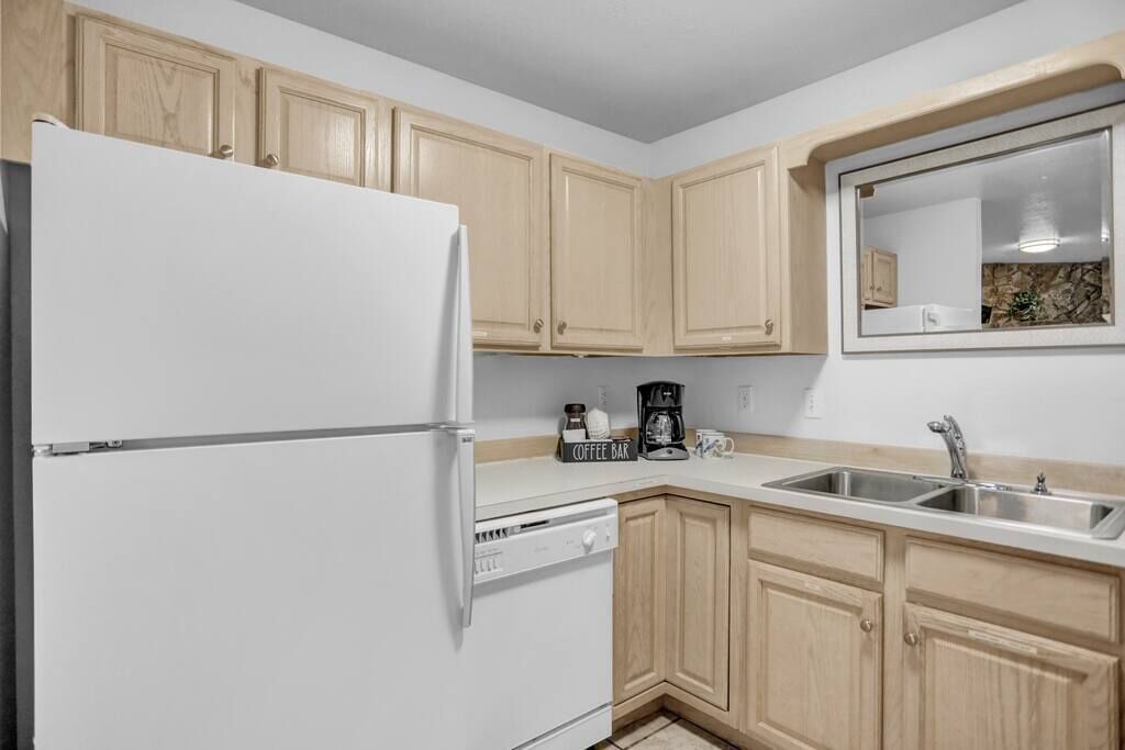 A kitchen with light wooden cabinets, a white refrigerator, a dishwasher, a coffee maker, and a sink.