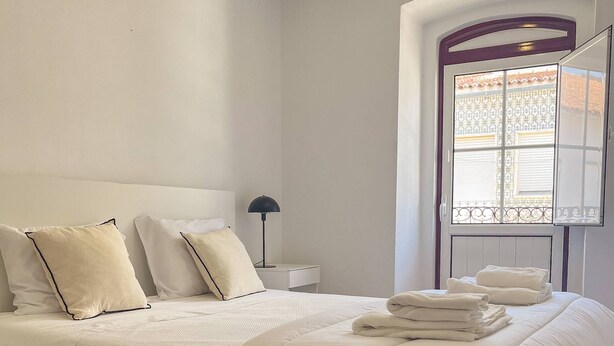 Un dormitorio con cama, mesita de noche, lámpara y ventana con vistas.