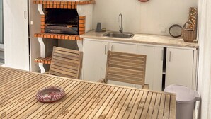 Cocina exterior con horno de ladrillo, lámpara colgante y platos decorativos en la pared.