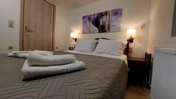 A hotel room with a bed, two bedside lamps, a painting on the wall, and a radiator. - Cozy suite, by Spyros & Marina, near to the city centre & old venetian harbour  (Chania)