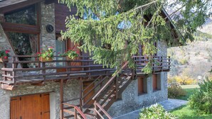 A stone building with a wooden staircase, wooden balcony railings, and potted plants. - Romito Lodge Apartment Mountain Retreat (Cesana Torinese)