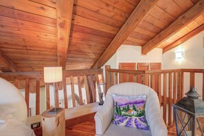 A wooden ceiling with exposed beams, a white upholstered chair with a colorful cushion, a small table with a lamp, and a lantern. - Romito Lodge Apartment Mountain Retreat (Cesana Torinese)