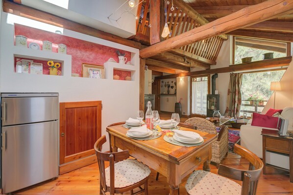 A wooden dining table set for four with chairs, a refrigerator, and a kitchen area in the background.