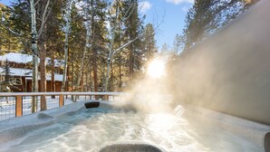 A hot tub surrounded by snow-covered ground and trees, with a wooden deck and a wooden cabin in the background. - Mountain Views from Private Hot Tub and Balcony and Large Windows (Keystone)