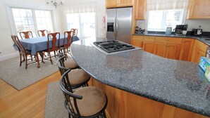 A kitchen with wooden cabinets, a stainless steel refrigerator, a gas stove, and a dining area with a blue tablecloth and chairs.