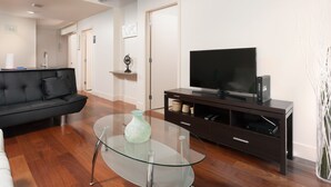 A modern living room with a glass coffee table, a black sofa, a flat-screen TV, and a dark wooden entertainment unit. - Pet Friendly 2 Bedroom And Apartment Near Rittenhouse Apts by RedAwning (Philadelphia)