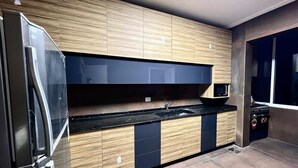 Eine moderne Küche mit Holzausstattung, einer schwarzen Arbeitsplatte und einem Edelstahlkühlschrank.
