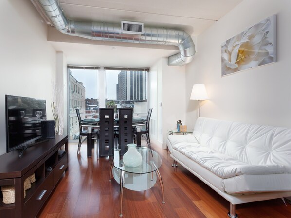 A modern living room with a white sofa, a glass coffee table, and a dining area with a black table and chairs. - Cozy Fully Furnished 2 Bedroom Apartment Apts by RedAwning (Philadelphia)