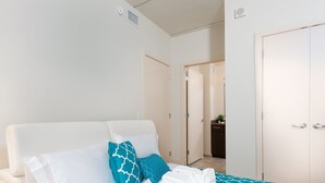 A bedroom with a bed, white walls, a bathroom with a sink, and a door.