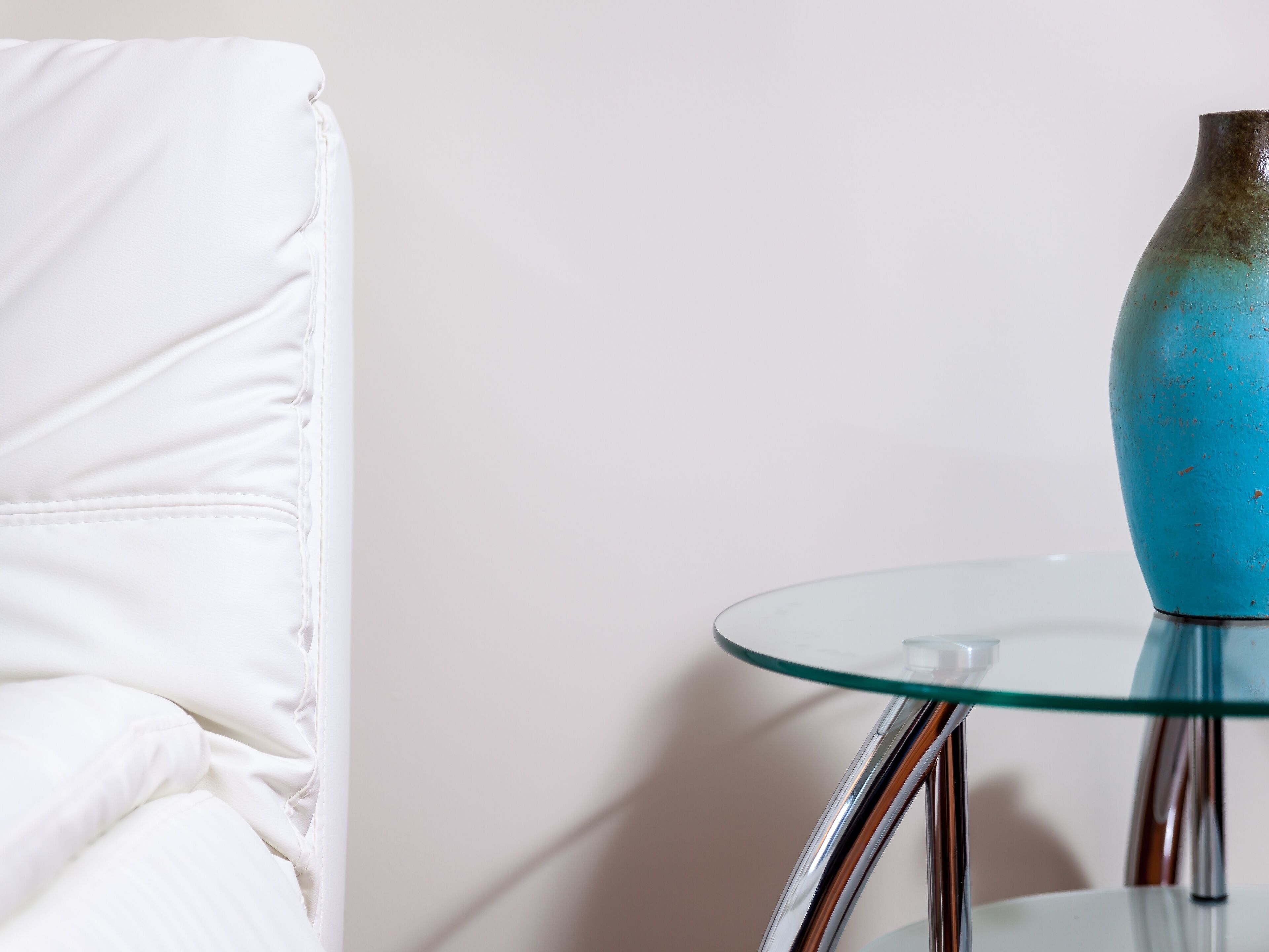 A white sofa and a glass table with a blue vase.
