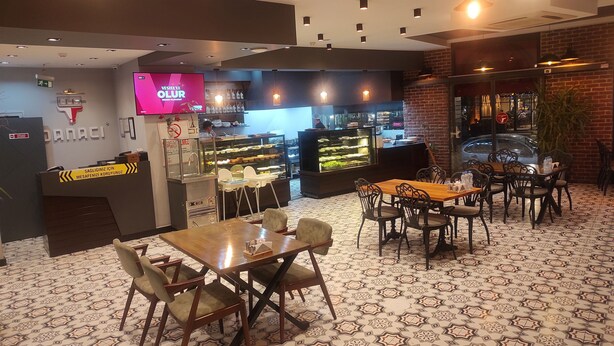 Um restaurante com piso estampado, um balcão com vitrine e uma tela de televisão.