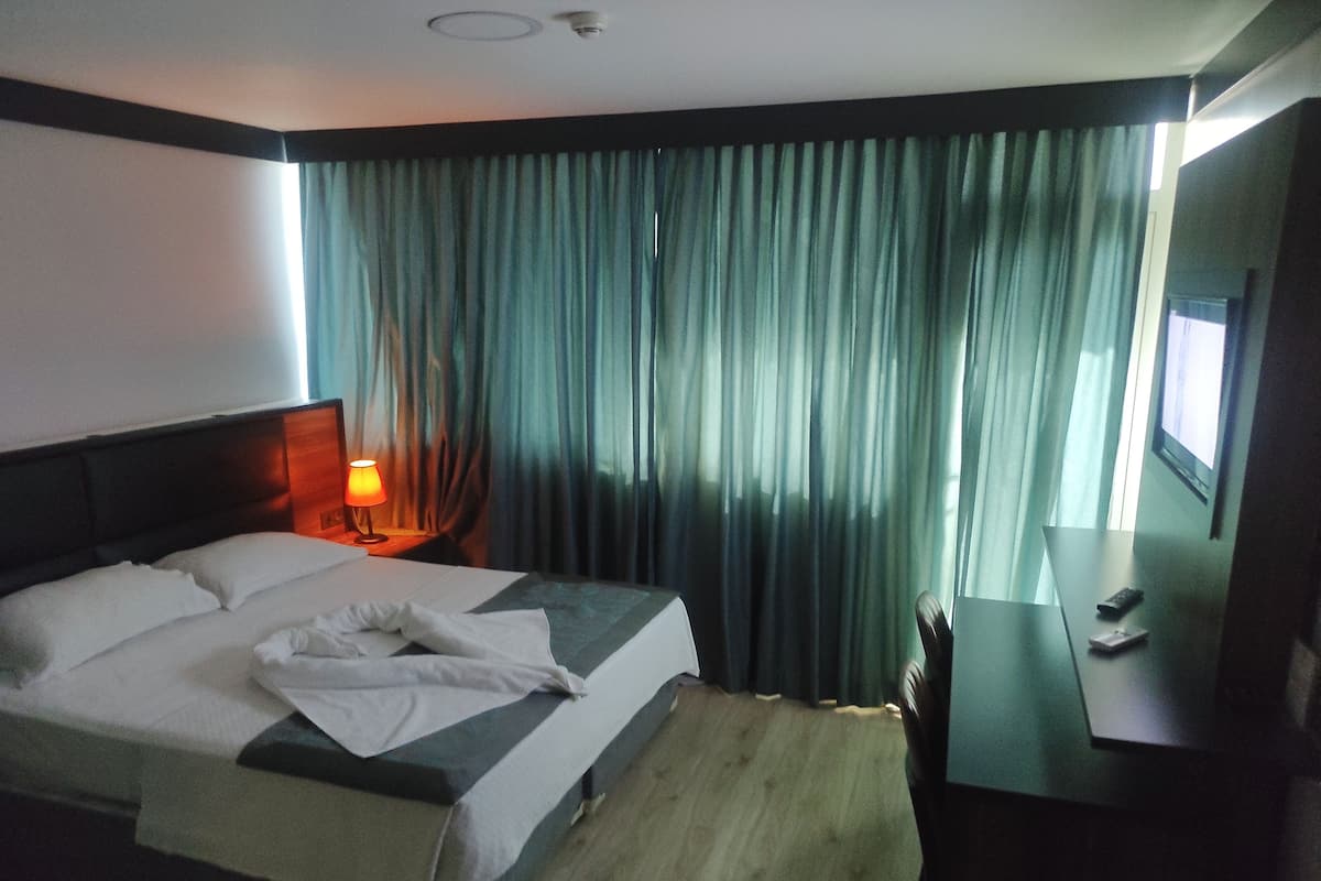 A hotel room with a bed, a nightstand with a lamp, a TV, and a window with curtains.