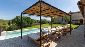 Un área junto a la piscina con sillones de descanso y una pérgola.