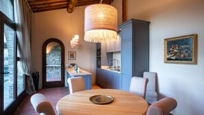 Un comedor con una mesa redonda de madera, sillas acolchadas, una lámpara colgante y una pared de piedra.
