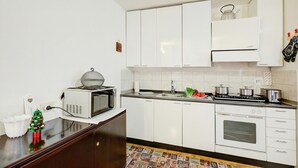 A kitchen with white cabinets, a microwave, a stove, and a small Christmas tree. - Studio Saturno 23 in the City Center (Sauze d'Oulx)