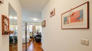A hallway with a wooden floor, a dining area with chairs and a table, and a bed in the background. - Studio Saturno 23 in the City Center (Sauze d'Oulx)