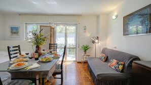 A dining area with a table set for two, a sofa, a potted plant, and a painting on the wall. - Studio Saturno 23 in the City Center (Sauze d'Oulx)