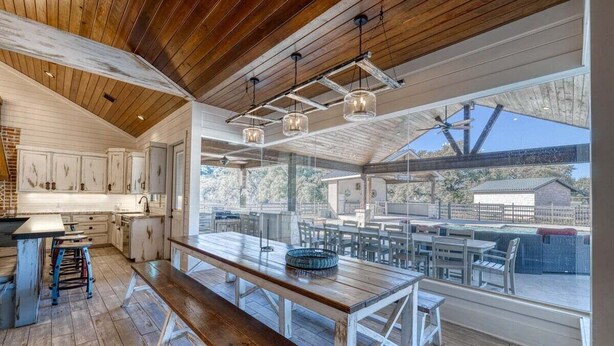 A modern kitchen with wooden cabinets, a large wooden table, and a view of the outdoor patio area.