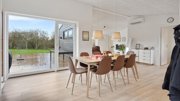 Ein geräumiger Essbereich mit Holztisch und Stühlen, einem großen Fenster und Blick auf einen Garten.