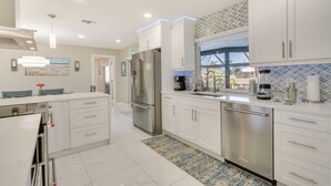 A modern kitchen with white cabinetry, stainless steel appliances, and a patterned backsplash. - Screened Lanai w/ TV: Waterfront Cape Coral Home! (Cape Coral)