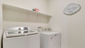 Une buanderie équipée d’un lave-linge et d’un sèche-linge Samsung, avec une étagère au-dessus du lave-linge et un panneau indiquant qu’il s’agit d’une laverie en libre-service, accessible 24 heures sur 24.