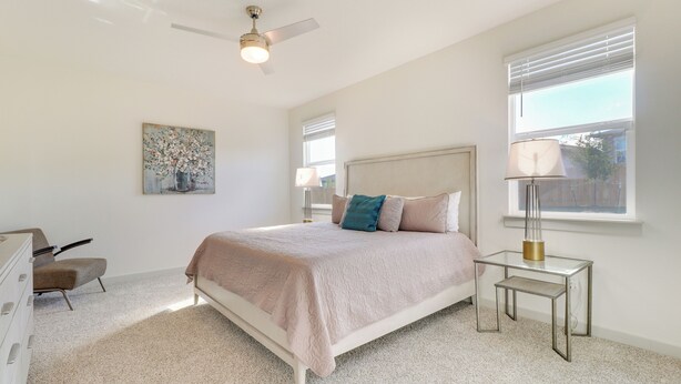 Une chambre à coucher avec un lit, un ventilateur de plafond, une table de chevet avec une lampe, une commode et un tableau au mur.
