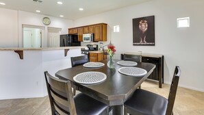 A modern kitchen with wooden cabinets, a microwave, and a stove. There is a dining table with placemats and chairs. - Spacious Surprise Home w/ Outdoor Pool + Game Room (Surprise)