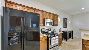 A kitchen with wooden cabinets, a stainless steel refrigerator, a microwave, a stove, and a coffee maker. - Spacious Surprise Home w/ Outdoor Pool + Game Room (Surprise)