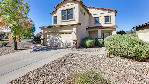 A two-story house with a garage, surrounded by a gravel driveway and landscaped with shrubs and trees. - Spacious Surprise Home w/ Outdoor Pool + Game Room (Surprise)