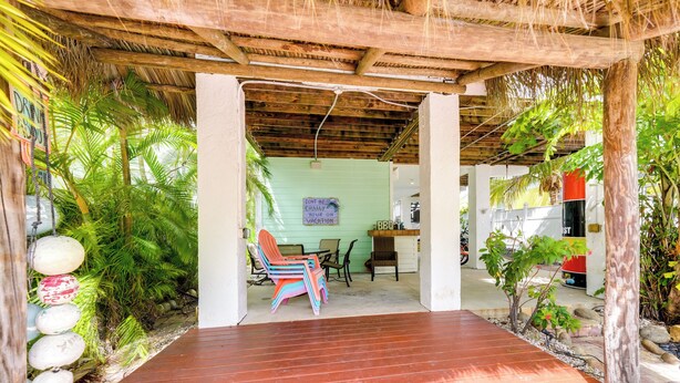 A wooden deck with a thatched roof, surrounded by tropical plants and a small seating area with colorful chairs. - Waterfront Key West Oasis w/ Float Dock! (Key West)