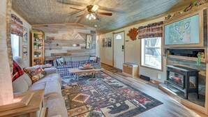 Un salon chaleureux avec une cheminée, un ventilateur de plafond et un grand tapis.