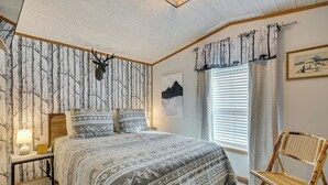 Une chambre à coucher comprenant un lit, une table de chevet, une lampe, une chaise, une décoration représentant une tête de cerf et une fenêtre avec des rideaux.
