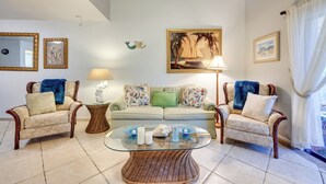 A living room with a light green sofa, two wicker armchairs, a glass coffee table, and a painting of a sailboat. - Serene St Augustine Townhome: Walk to Beach! (St. Augustine)
