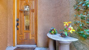 A wooden door with a welcome mat, a small table with potted plants, and a textured wall. - Serene St Augustine Townhome: Walk to Beach! (St. Augustine)
