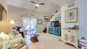 A spacious living room with a sofa, a glass coffee table, a blue cabinet, and a ceiling fan. - Serene St Augustine Townhome: Walk to Beach! (St. Augustine)